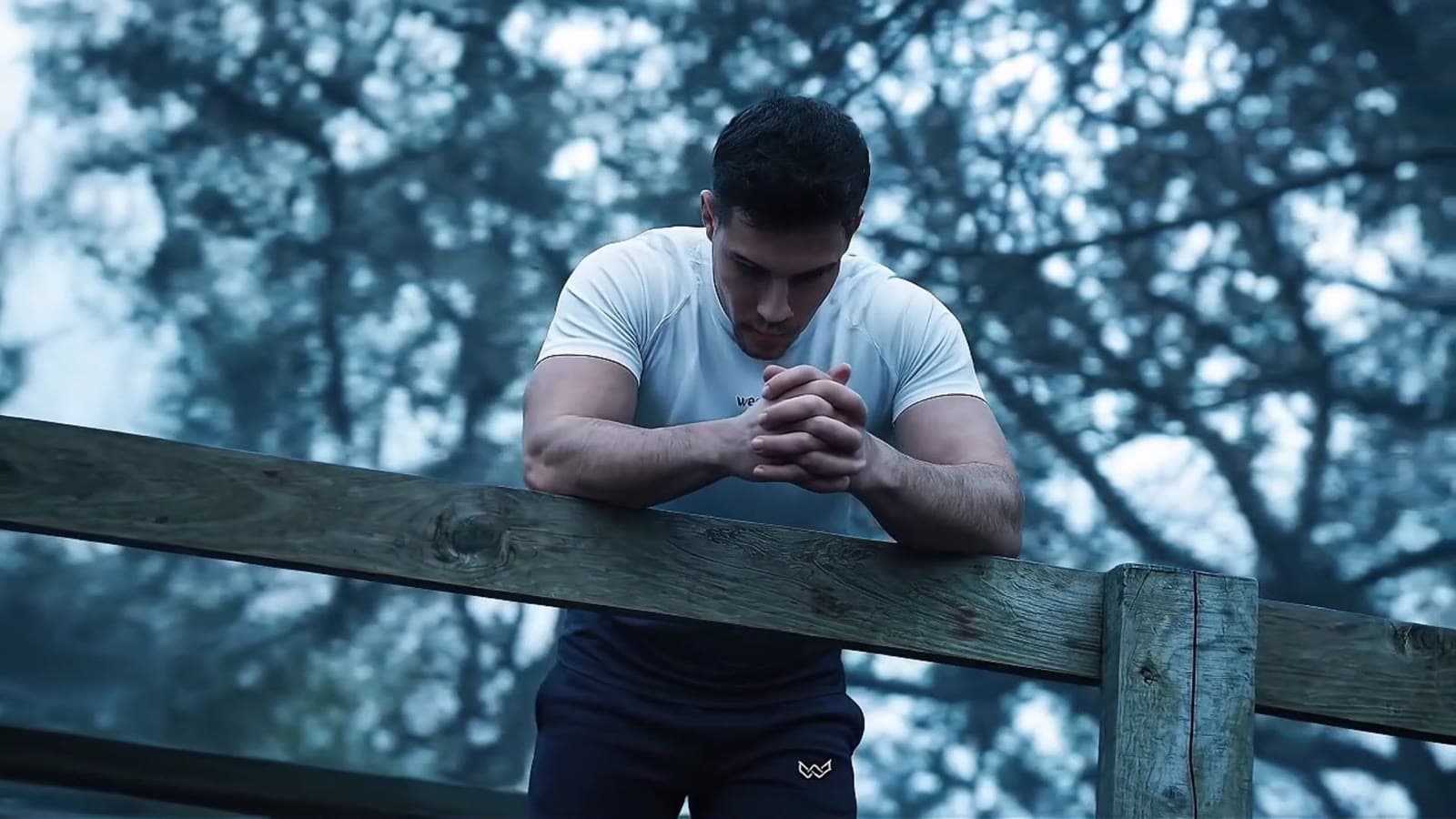 Man leaning on a wooden fence in a misty forest, from an AI activewear film